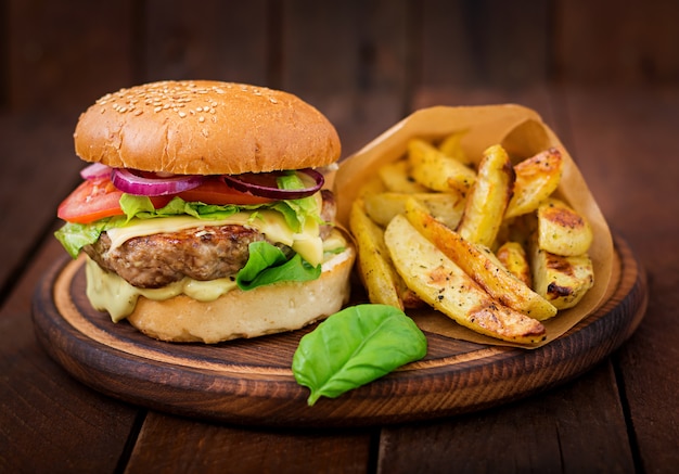 Большой бутерброд - гамбургер с сочным говяжьим гамбургером, сыром, помидорами и красным луком на деревянном столе