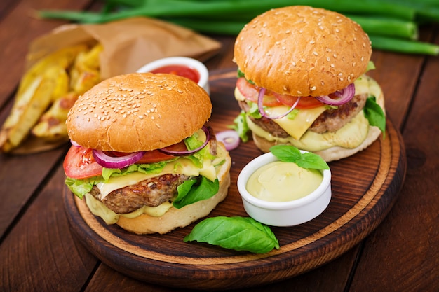 Большой бутерброд - гамбургер с сочным говяжьим гамбургером, сыром, помидорами и красным луком на деревянном столе