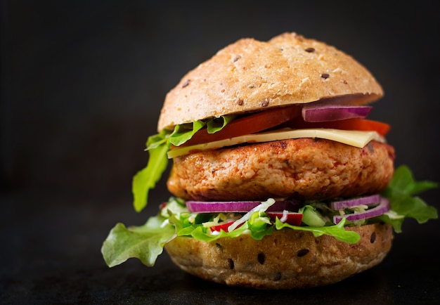 Большой бутерброд - гамбургер с сочным куриным бургером, сыром, помидорами и красным луком на черном столе