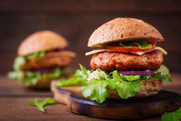 Большой бутерброд - гамбургер с сочным куриным бургером, сыром, помидорами и красным луком на деревянном столе