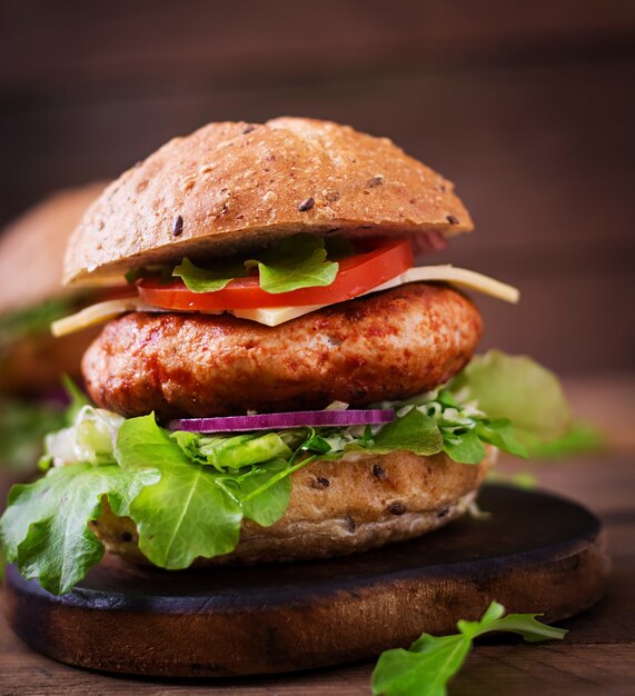 Big sandwich - hamburger with juicy chicken burger, cheese, tomato, and red onion on wooden table