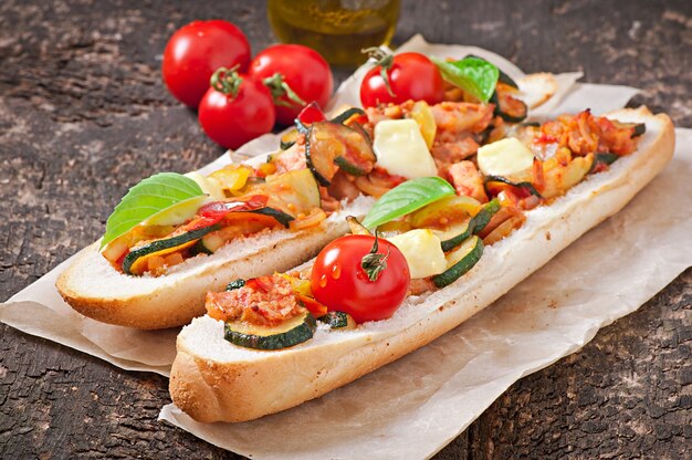 Big sandwich with roasted vegetables with cheese and basil on old wooden surface