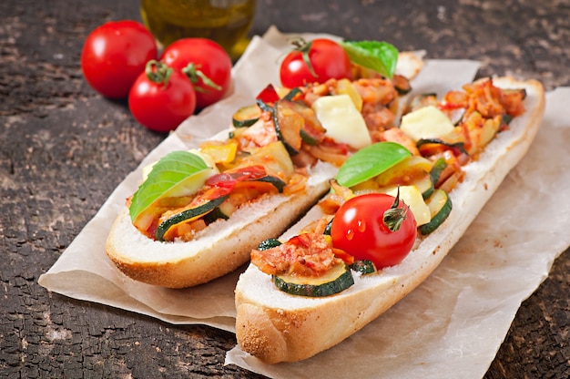 Big sandwich with roasted vegetables with cheese and basil on old wooden surface