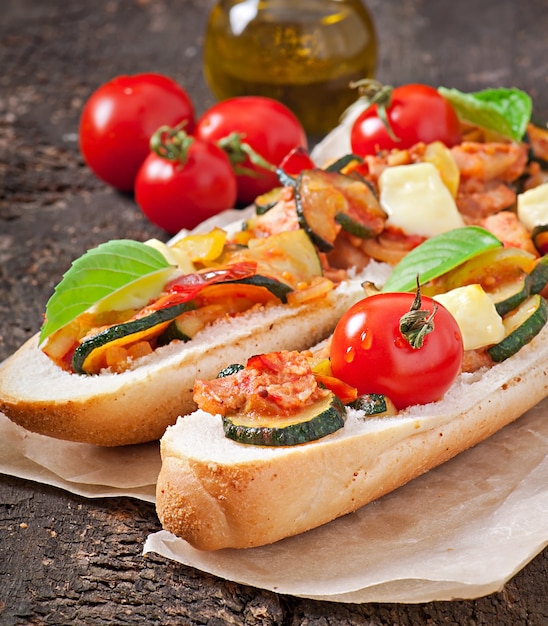 Big sandwich with roasted vegetables with cheese and basil on old wooden surface