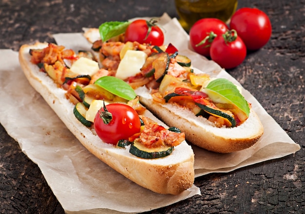 Big sandwich with roasted vegetables with cheese and basil on old wooden surface