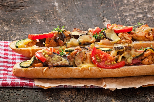 Big sandwich with roasted vegetables (zucchini, eggplant, tomatoes) with cheese and thyme on old wooden background