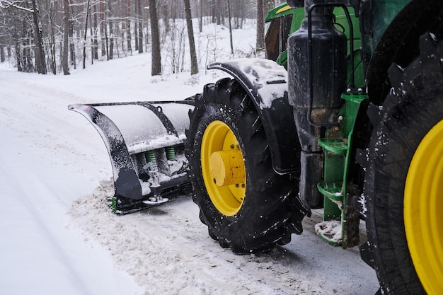 Большой специальный трактор убирает снег с лесной дороги.