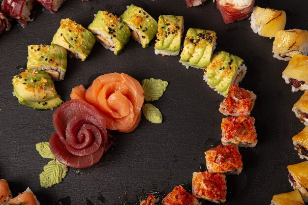 Большой выбор суши-роллов и кусочков лосося в форме роз на черной поверхности