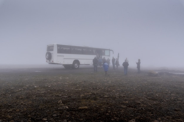 アイスランドの霧深い天気で大きな白いバスとその近くの人々のグループ