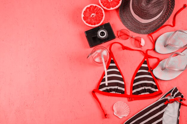 Bikini; hat; camera; flippers; sunglasses; juice and halved grapefruit on pink textured backdrop