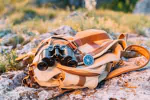 Foto gratuita binocolo, bussola e borsa su roccia