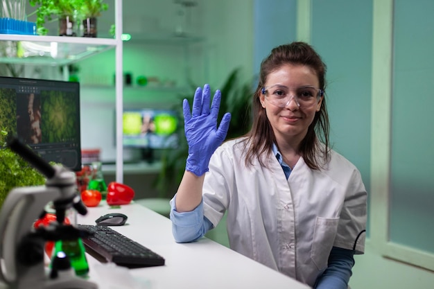 Foto gratuita donna biochimica che saluta uno scienziato remoto che discute il test dell'esperimento di microbiologia durante la conferenza videochiamata online. medico ricercatore che lavora in laboratorio biologico. teleconferenza