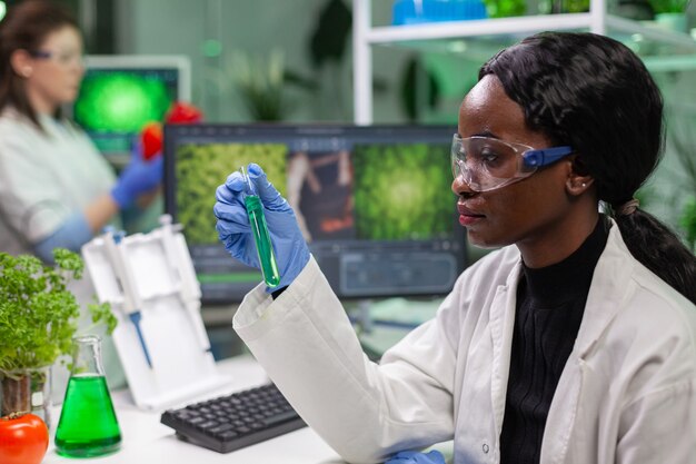 Биолог держит пробирку с генетической жидкостью, исследуя образец зеленой ДНК для биохимической экспертизы
