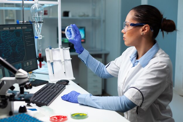 파란색 용액을 분석하는 투명한 페트리 접시를 들고 있는 생물학자 연구원 여성