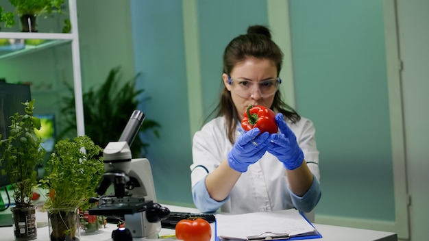 Foto gratuita donna biologa che esamina pepe che scrive competenza medica di microbiologia sul blocco note