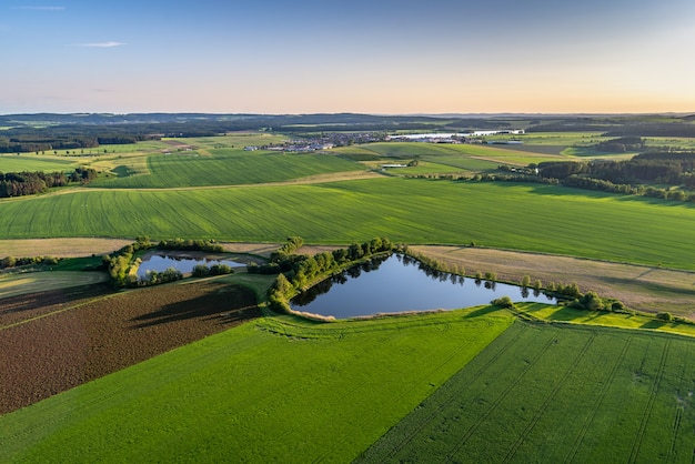 Bird's-eye shot of breathtaking green fields with small ponds in a rural area