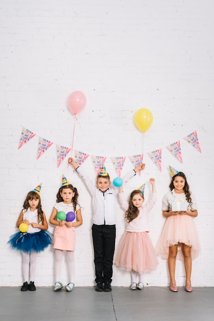 Birthday boy standing with girls against white wall decorated with bunting