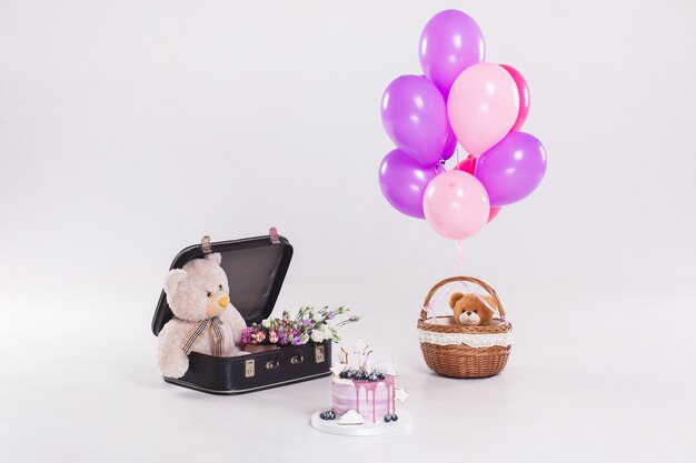 Birthday cake, teddy bear in vintage suitecase and balloons isolated on white background