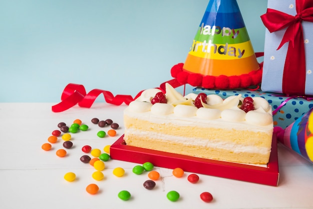 Birthday cake with candies; hat; and presents on table against blue backdrop