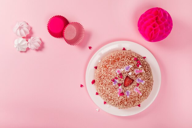 Birthday cake with candles; zephyrs; paper cupcake holder and honeycomb pom-pom paper balls on pink backdrop