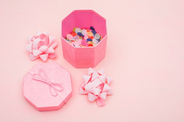 Концепция дня рождения с конфетти в подарочной коробке, банты на розовом фоне высокого угла зрения.