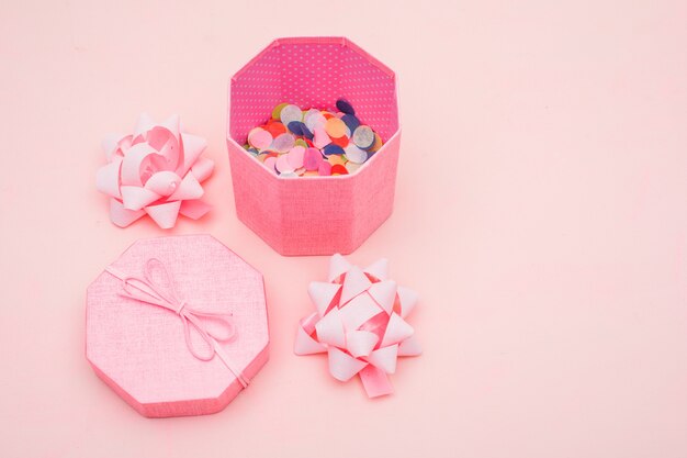 Birthday concept with confetti in gift box, bows on pink background high angle view.