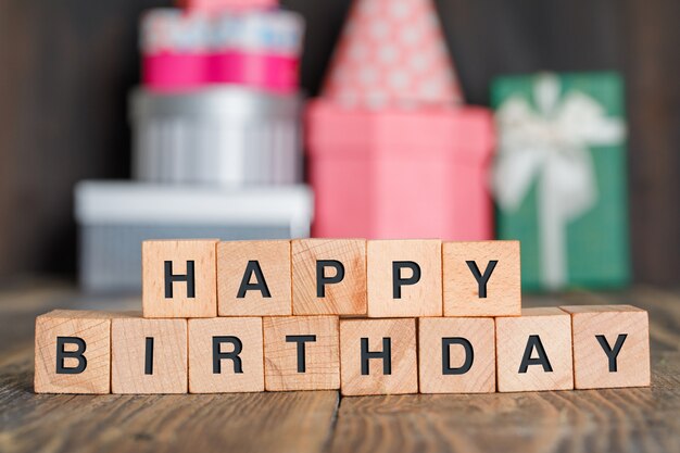 Birthday concept with gift boxes, wooden cubes on wooden table side view.