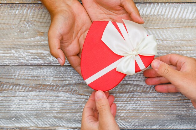 Birthday concept on wooden background flat lay. hands giving and receiving present box.