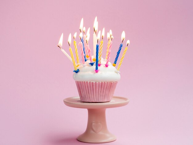 Birthday muffin with colorful candles on pink background