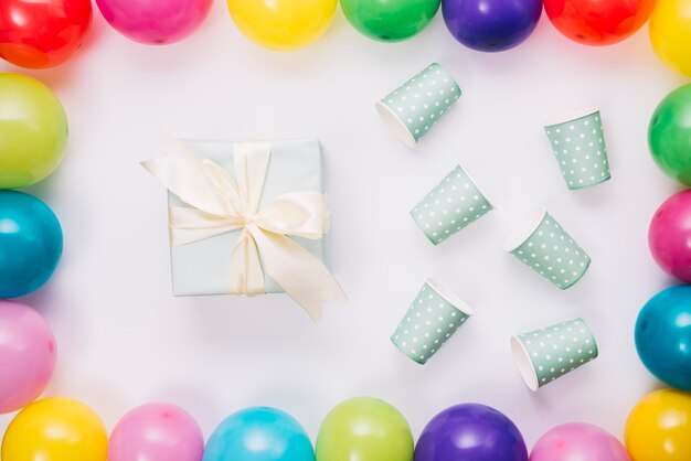 Birthday present and disposable cup inside the balloons border on white background