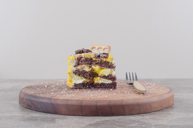 Biscuit and anise on a cake slice next to a fork on a board on marble 