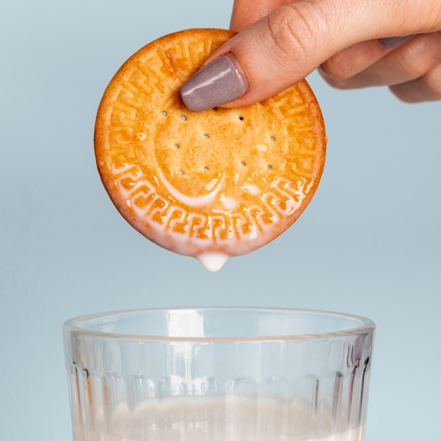 Biscuit held above glass of milk close-up