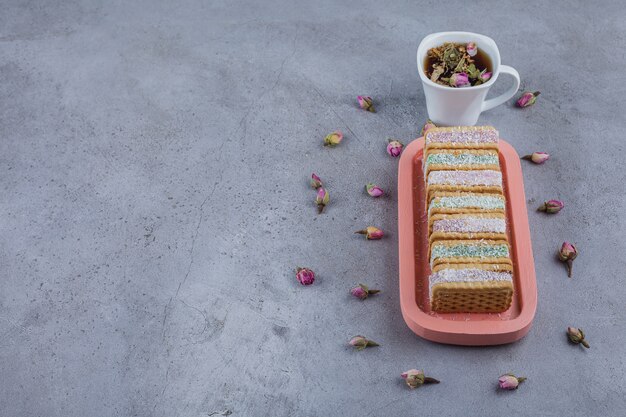 Biscuit sandwich filled with colorful marmalade on pink plate and cup of tea.