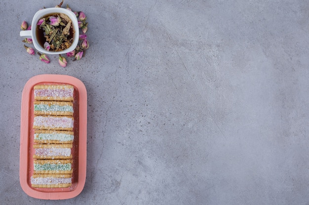 Biscuit sandwich filled with colorful marmalade on pink plate and cup of tea. 