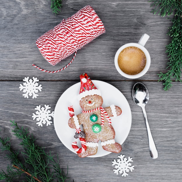 Biscuit snowman on plate near cup of drink, snowflakes and threads 