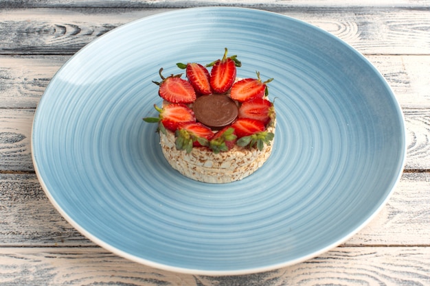 biscuit with strawberries and round chocolate inside blue plate on rustic grey