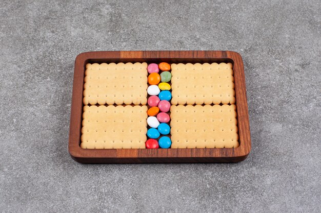 Biscuits and colorful candies on wooden plate