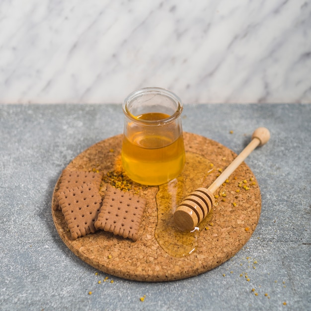 Foto gratuita biscotti e vasetto di miele con mestolo in legno su sottobicchiere di sughero sullo sfondo di granito