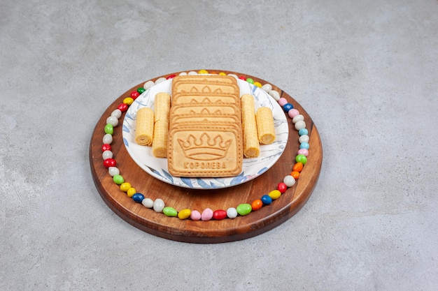 Biscuits lined up on a plate and surrounded by candies on wooden board on marble background. High quality photo