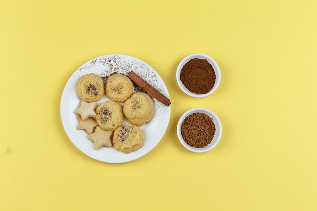 Печенье на тарелке с кофе, палочка корицы на желтом фоне