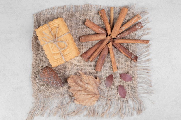 Free photo biscuits in rope with cinnamon sticks, leaf and pinecone on burlap. high quality photo