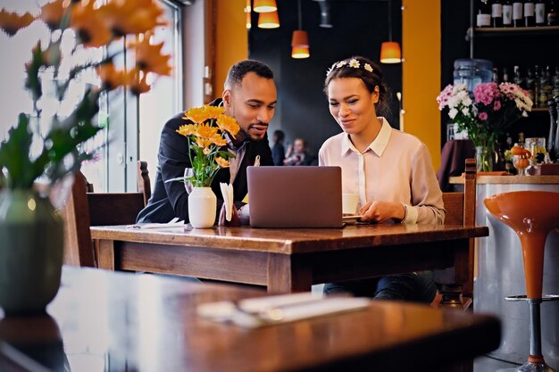 Black African American business male and female drinks coffee and using a laptop in a restaurant.