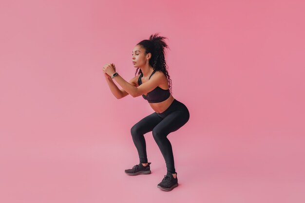 black african american woman in black leggings and top fitness outfit on pink