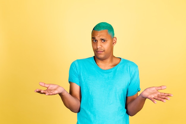 Black african man in casual on yellow wall look to camera shrugging shoulders clueless and confused