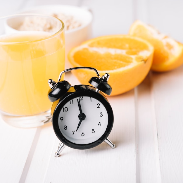 Черный будильник с апельсиновым соком в стекле на столе