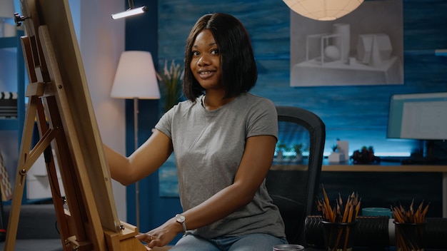 Black artistic woman sitting in workshop studio and drawing vase with pencil on white canvas. African american young artist working on modern masterpiece with art tools and instruments