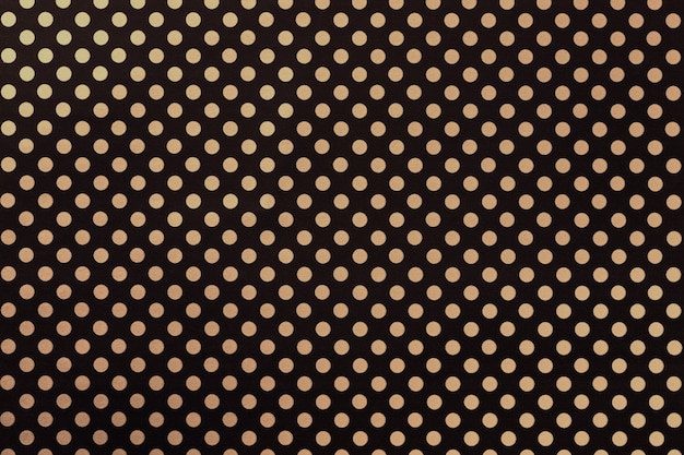 黄金​の​水玉​の​クローズアップ​の​パターン​を​持つ​包装紙​から​黒​の​背景​。