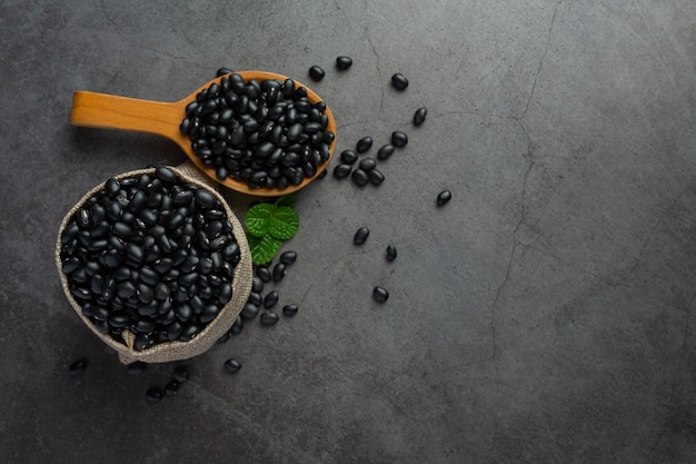 Foto gratuita fagiolo nero in un piccolo cucchiaio di legno posto accanto al sacco pieno di fagioli neri