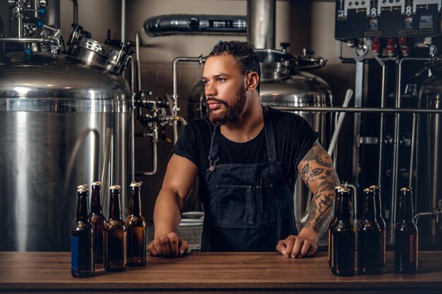 Чернобородый татуированный хипстер-производитель, представляющий крафтовое пиво в пивоварне.