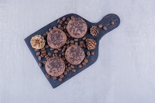 Black board with coffee beans, cookies, and pine cones on white background.